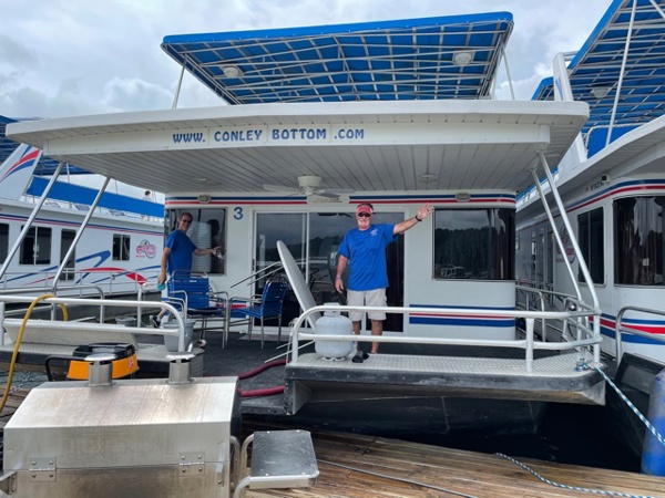 Two Conley Bottom Resort staff members aboard a large houseboat's back deck.