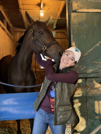 Annise Montplaisir, Executive Director of Amplify Horse Racing posing with a brown horse.