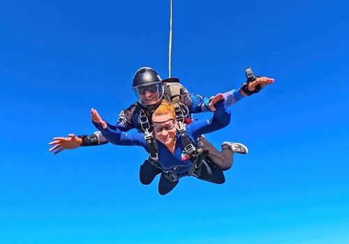 Skydiving instructor and student in tandem freefall, arms outstretched while descending against a blue sky.
